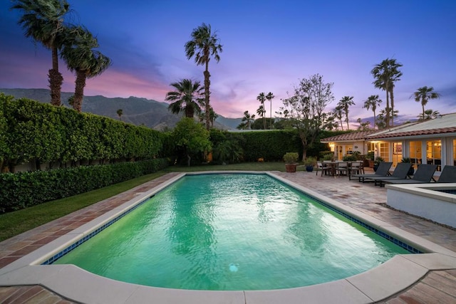 pool at dusk featuring a mountain view and a patio