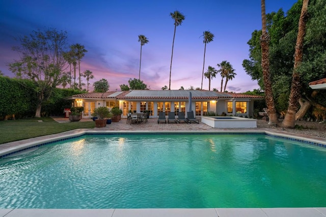 pool at dusk featuring a hot tub and a patio