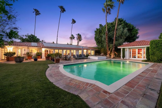 pool at dusk featuring a yard, a patio area, and an outdoor structure