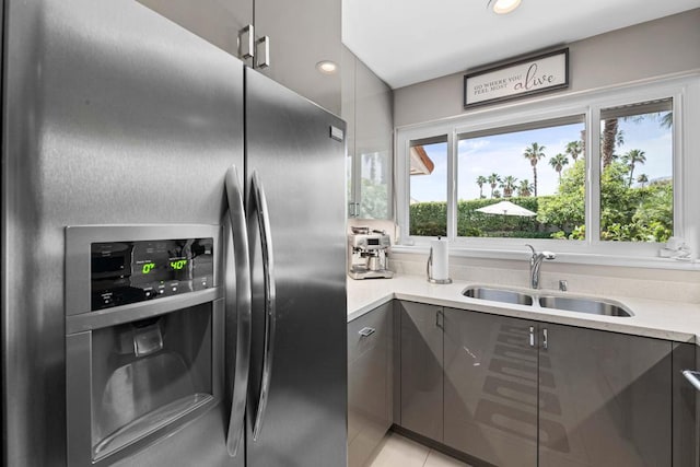 kitchen with light tile patterned floors, sink, stainless steel fridge, and gray cabinetry