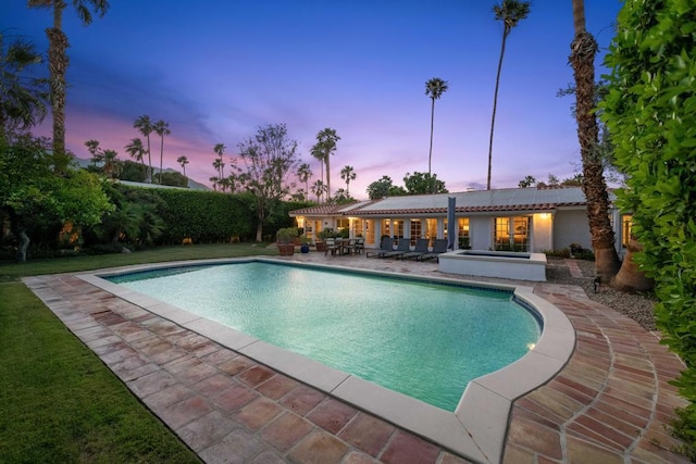 pool at dusk featuring an in ground hot tub and a patio