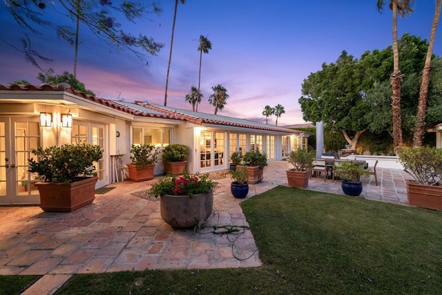 back house at dusk with a lawn, french doors, and a patio