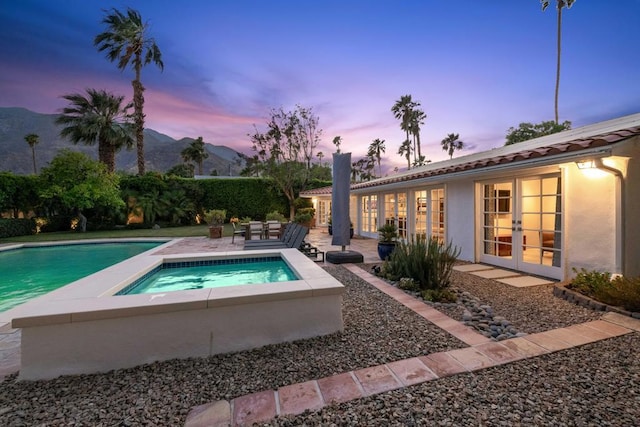 pool at dusk with an in ground hot tub, a mountain view, french doors, and a patio