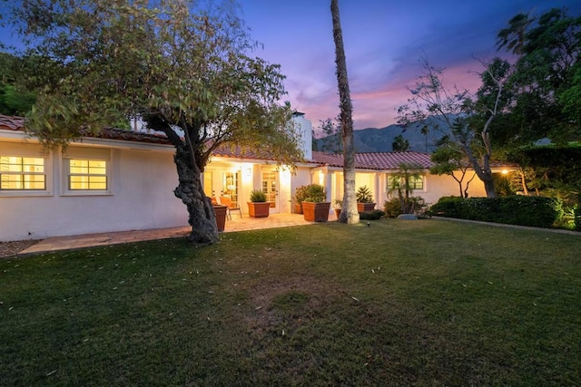 back house at dusk featuring a patio area and a yard