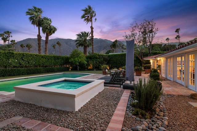 pool at dusk featuring a mountain view, a patio area, an in ground hot tub, and french doors