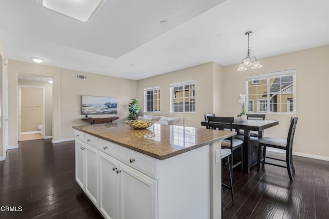 kitchen with dark wood-type flooring, white cabinetry, dark stone countertops, a kitchen island, and decorative light fixtures