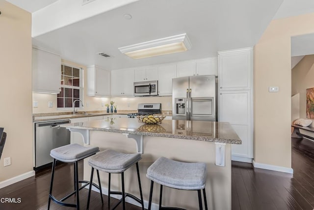 kitchen featuring white cabinetry, appliances with stainless steel finishes, a center island, and dark wood-type flooring