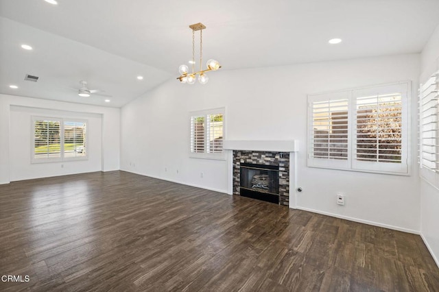 unfurnished living room featuring ceiling fan with notable chandelier, dark wood-type flooring, a wealth of natural light, and a fireplace