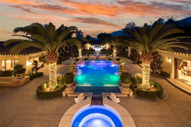 pool at dusk with a patio and an in ground hot tub