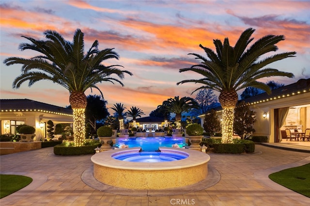 pool at dusk with a patio area and an in ground hot tub