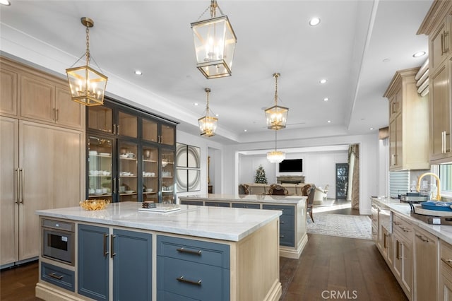 kitchen with light stone countertops, hanging light fixtures, dark hardwood / wood-style floors, a raised ceiling, and a large island