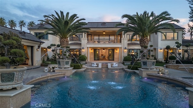 pool at dusk featuring pool water feature and a patio