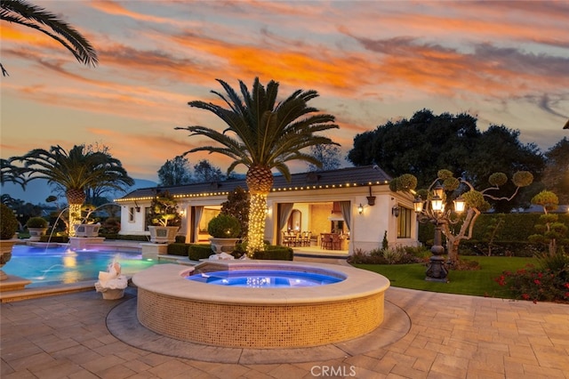 pool at dusk with pool water feature, a patio area, and an in ground hot tub