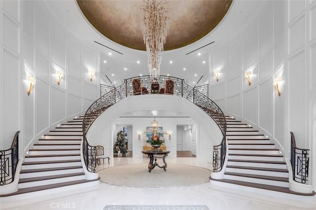 stairs with a high ceiling, a raised ceiling, and an inviting chandelier