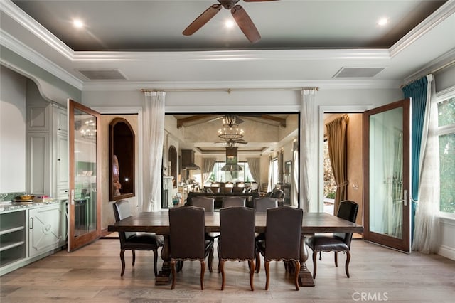 dining room with a raised ceiling, ceiling fan with notable chandelier, ornamental molding, and light hardwood / wood-style flooring