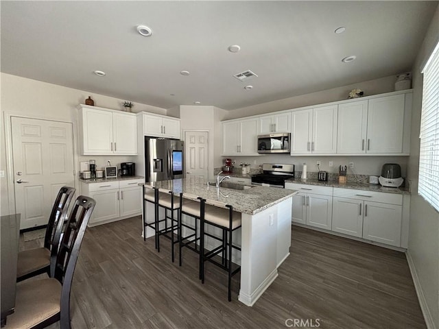 kitchen featuring white cabinets, a kitchen bar, dark hardwood / wood-style flooring, stainless steel appliances, and a kitchen island with sink