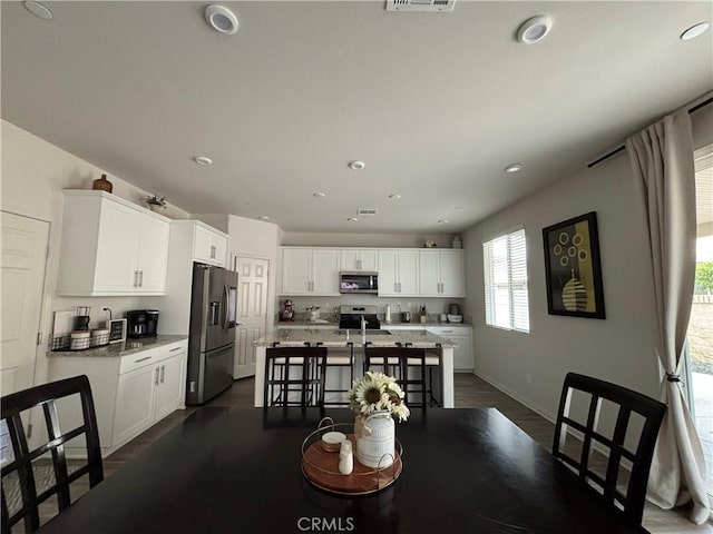 kitchen with light stone countertops, appliances with stainless steel finishes, white cabinetry, and a kitchen island with sink