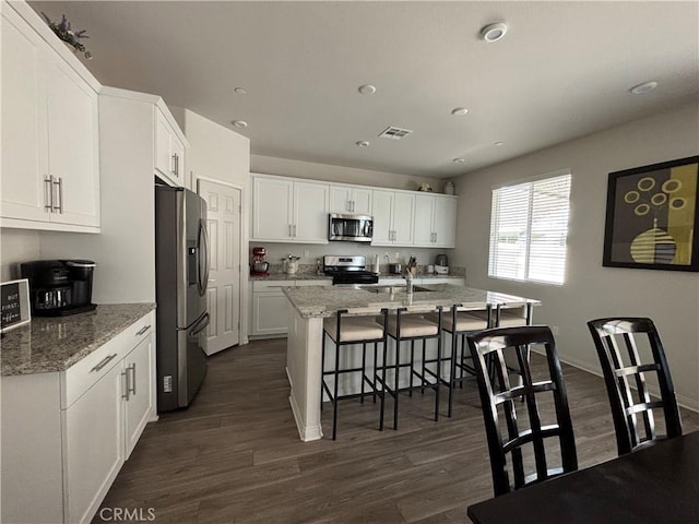 kitchen featuring stainless steel appliances, dark hardwood / wood-style floors, a kitchen island with sink, white cabinets, and light stone counters