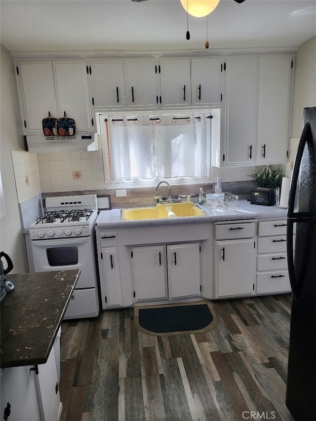 kitchen with white cabinets, dark wood-type flooring, black refrigerator, sink, and white gas range oven