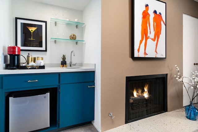 bar featuring light stone countertops, sink, fridge, and blue cabinets