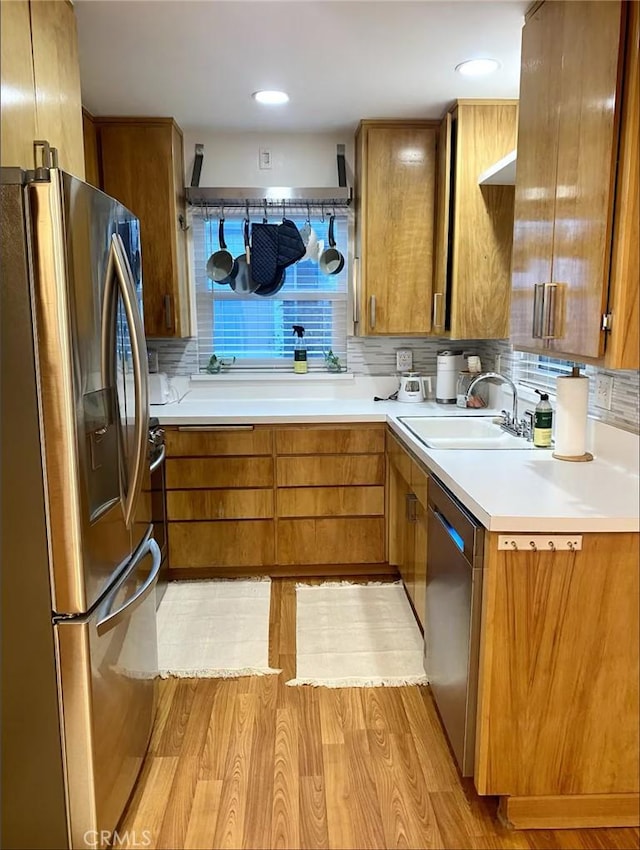 kitchen with tasteful backsplash, light wood-type flooring, appliances with stainless steel finishes, and sink