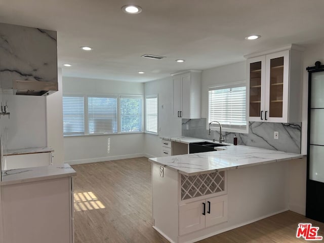 kitchen featuring kitchen peninsula, light wood-type flooring, white cabinets, light stone counters, and sink