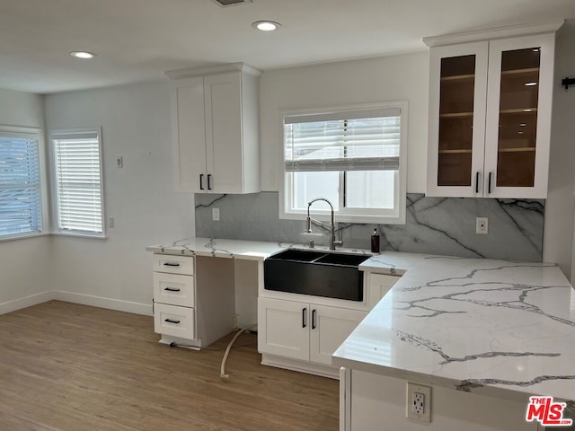 kitchen with light stone countertops, a wealth of natural light, white cabinets, and sink