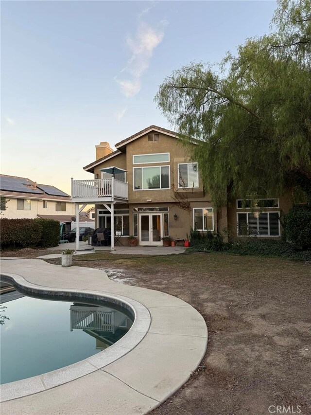 back house at dusk with a patio area, a balcony, and french doors