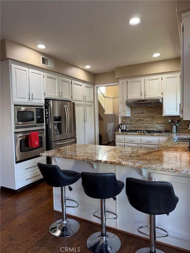 kitchen featuring kitchen peninsula, decorative backsplash, white cabinetry, light stone countertops, and stainless steel appliances