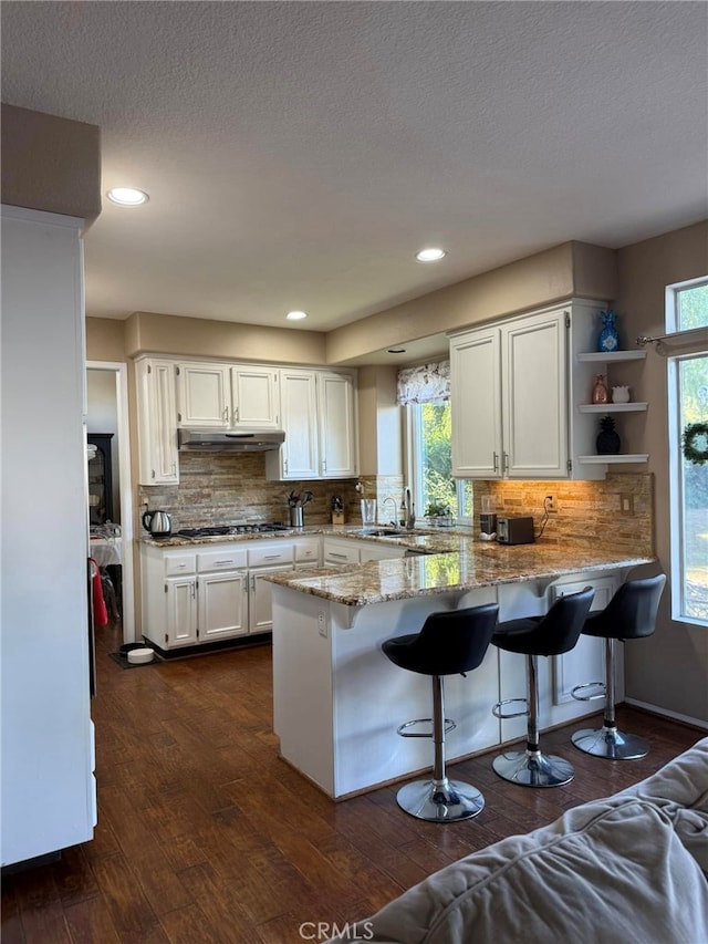 kitchen with stainless steel gas cooktop, kitchen peninsula, light stone countertops, and white cabinetry