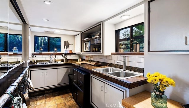 kitchen with white cabinetry, kitchen peninsula, backsplash, white gas stovetop, and sink