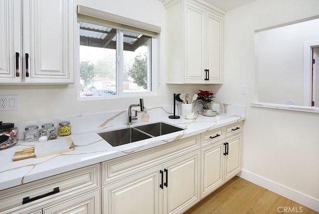 kitchen featuring light stone countertops, white cabinetry, light hardwood / wood-style flooring, and sink