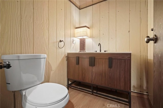 bathroom featuring toilet, vanity, wood walls, and hardwood / wood-style floors