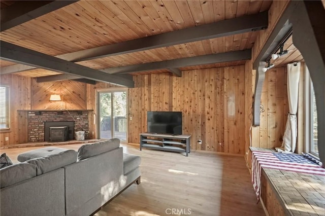 living room with wood walls, wooden ceiling, a wood stove, light hardwood / wood-style flooring, and beamed ceiling