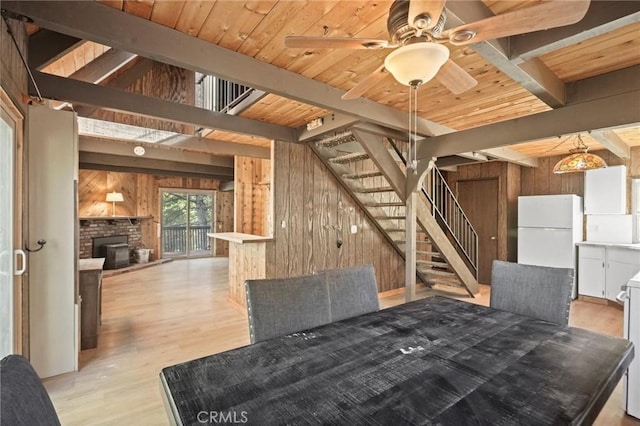 unfurnished dining area featuring a brick fireplace, beam ceiling, ceiling fan, and wooden walls