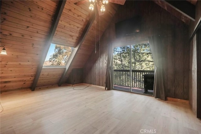 additional living space with vaulted ceiling with skylight, wood ceiling, wooden walls, light wood-type flooring, and ceiling fan