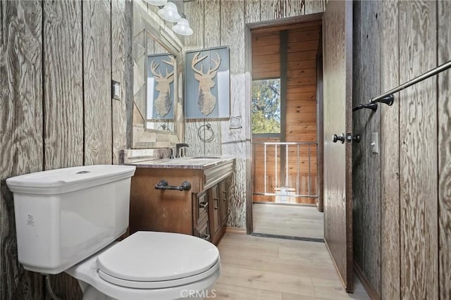 bathroom featuring hardwood / wood-style floors, toilet, vanity, and wood walls