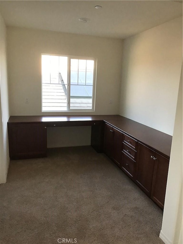 unfurnished office featuring built in desk and light colored carpet