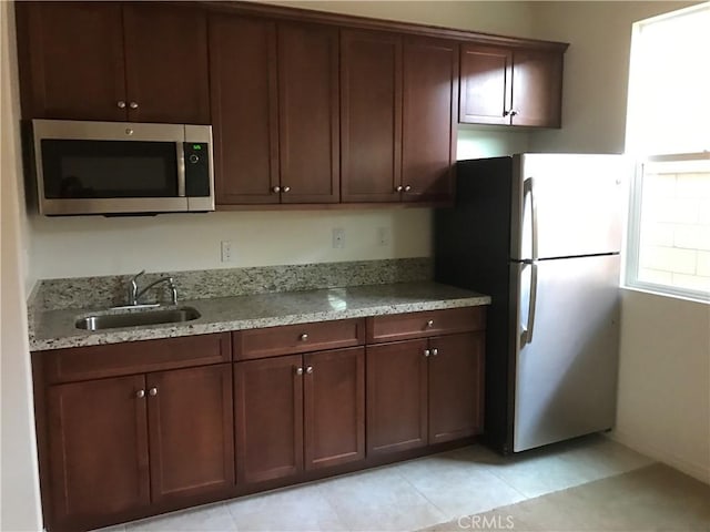 kitchen featuring light stone counters, sink, stainless steel appliances, and light tile patterned flooring