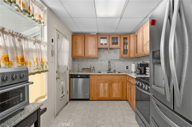 kitchen with light stone countertops, a paneled ceiling, appliances with stainless steel finishes, and sink