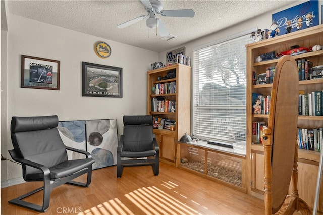 living area featuring ceiling fan, a textured ceiling, and light hardwood / wood-style floors