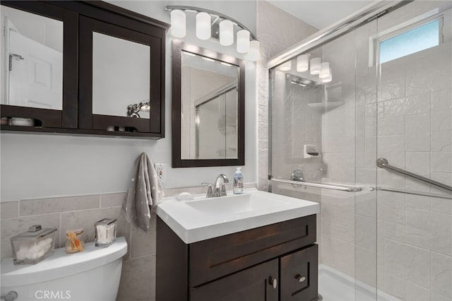 bathroom with toilet, tile walls, a shower with shower door, and vanity