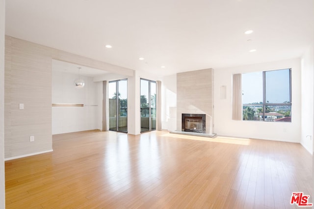 unfurnished living room featuring plenty of natural light, a tile fireplace, an inviting chandelier, and light hardwood / wood-style floors