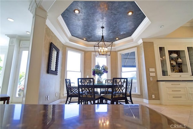 tiled dining space featuring a chandelier, a raised ceiling, ornamental molding, and ornate columns