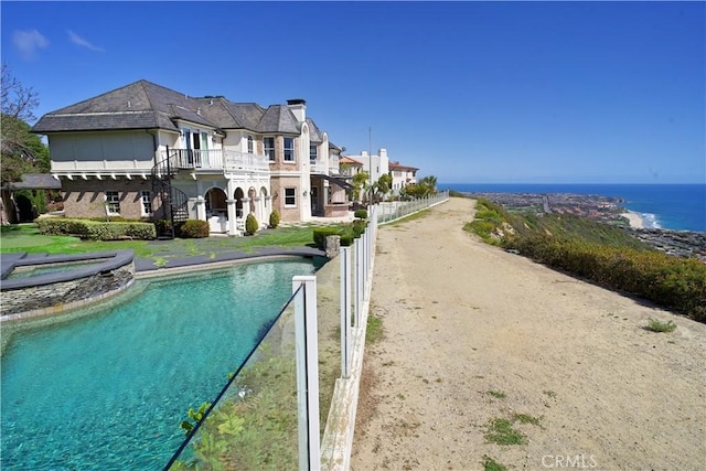 rear view of house with a water view, a fenced in pool, and a balcony