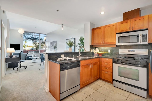 kitchen featuring kitchen peninsula, stainless steel appliances, light colored carpet, dark stone counters, and sink