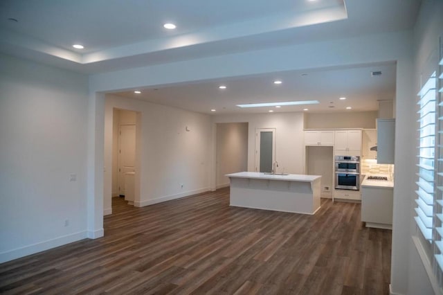 kitchen with stainless steel double oven, a center island with sink, sink, dark wood-type flooring, and white cabinets