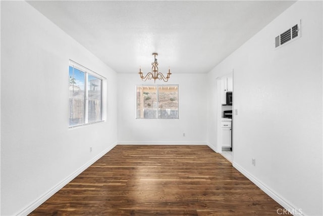 empty room with dark wood-type flooring and a notable chandelier