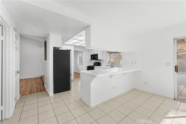 kitchen featuring black appliances, white cabinetry, kitchen peninsula, light tile patterned flooring, and a breakfast bar