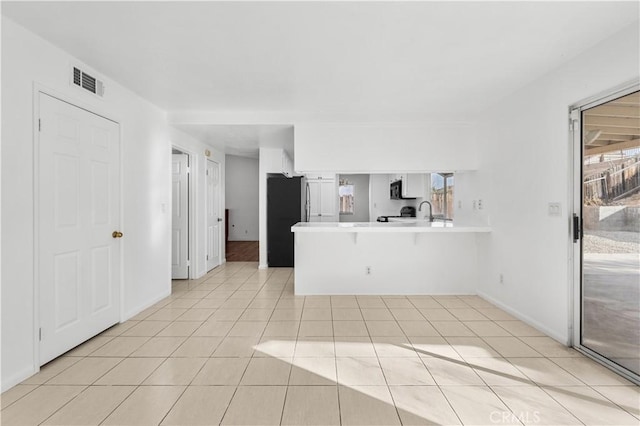 interior space featuring a breakfast bar area, light tile patterned flooring, kitchen peninsula, and stainless steel refrigerator